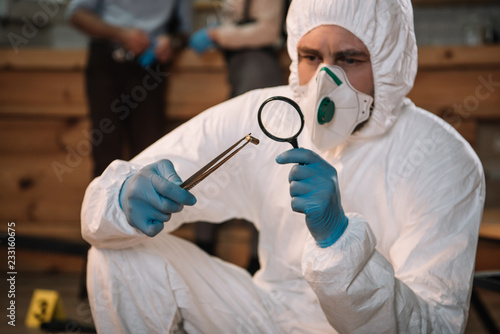 close up of forensic investigator examining evidence with magnifying glass at crime scene photo