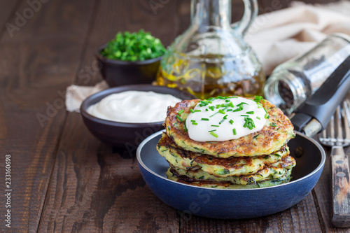 Vegetarian zucchini fritters or pancakes, served with greek yogurt and green onion, in little pan, horizontal, copy space