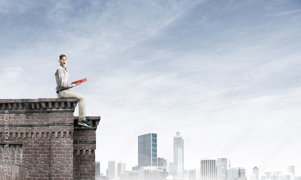 Man on roof edge reading book and cityscape at background Man on roof edge reading book and cityscape at background