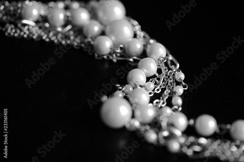 Necklace of white beads and metal chain on a dark background close up. Black and white