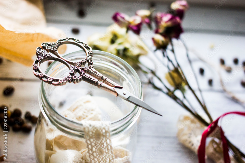 Vintage and handmade background. Decorative scissors for sewing on a glass jar with lace and braid on a wooden background