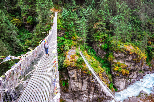 Woman backpacker crossing suspension bridge in Himalayas Nepal photo