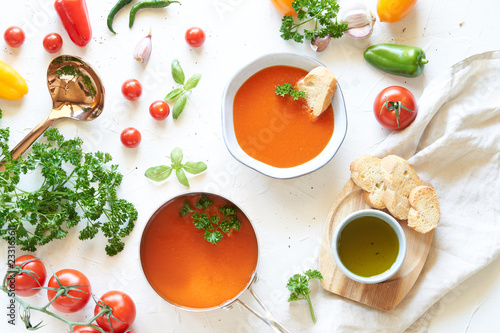 Gazpacho soup in metal pan and plate with fresh tomatoes, green sauce, chili, garlic, Basil and French baguette on white background. Top view