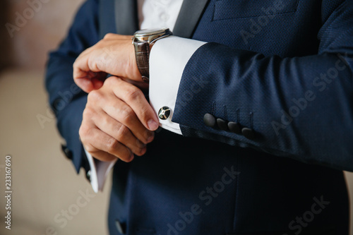 Closeup businessman puts on cufflinks and wristwatches, wears expensive leather belt. Man in a business suit, white shirt. Preparing the groom on the wedding day photo