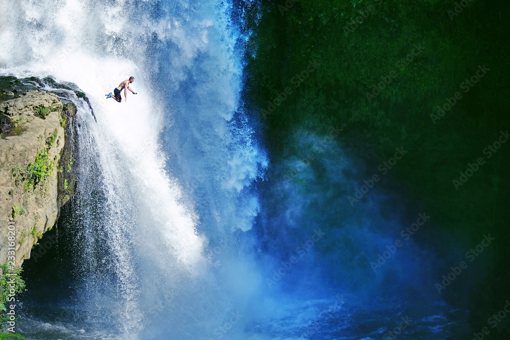 Obraz premium Jumping from the rock into the water. Man having fun at waterfalls in the nature. Bali, Indonesia