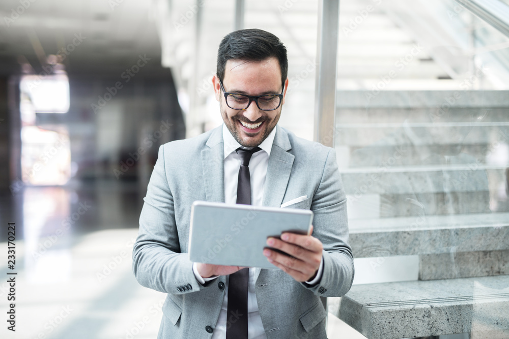 Portrait of businessman smiling and using tablet for work while leaning on the glass. In background staircase. Portrait of businessman smiling and using tablet for work while leaning on the glass. In background staircase.
