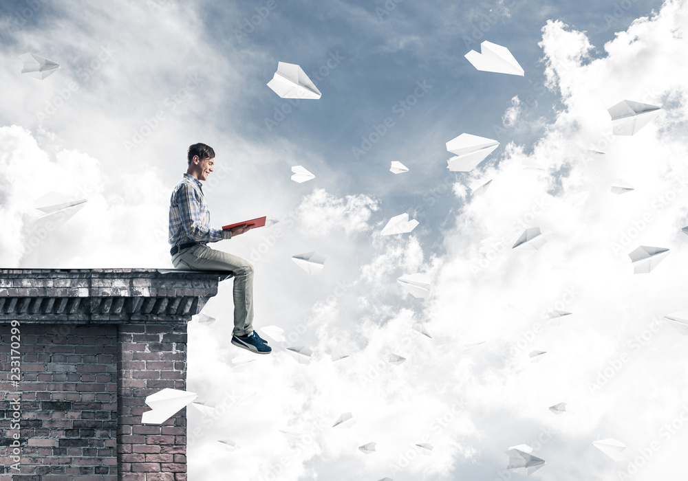 Handsome student guy on roof edge reading book and paper planes Handsome student guy on roof edge reading book and paper planes