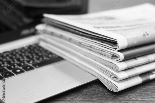 Newspapers and laptop. Pile of daily papers with news on the computer. Pages with headlines, articles folded and stacked on keypad of electronic device. Modern gadget and old journals, focus on paper 