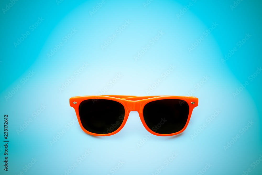 Summer orange sunglasses isolated in vignetting blue background. Minimal concept image for sun protection, hot days, tropical travel, summer vacation holidays.