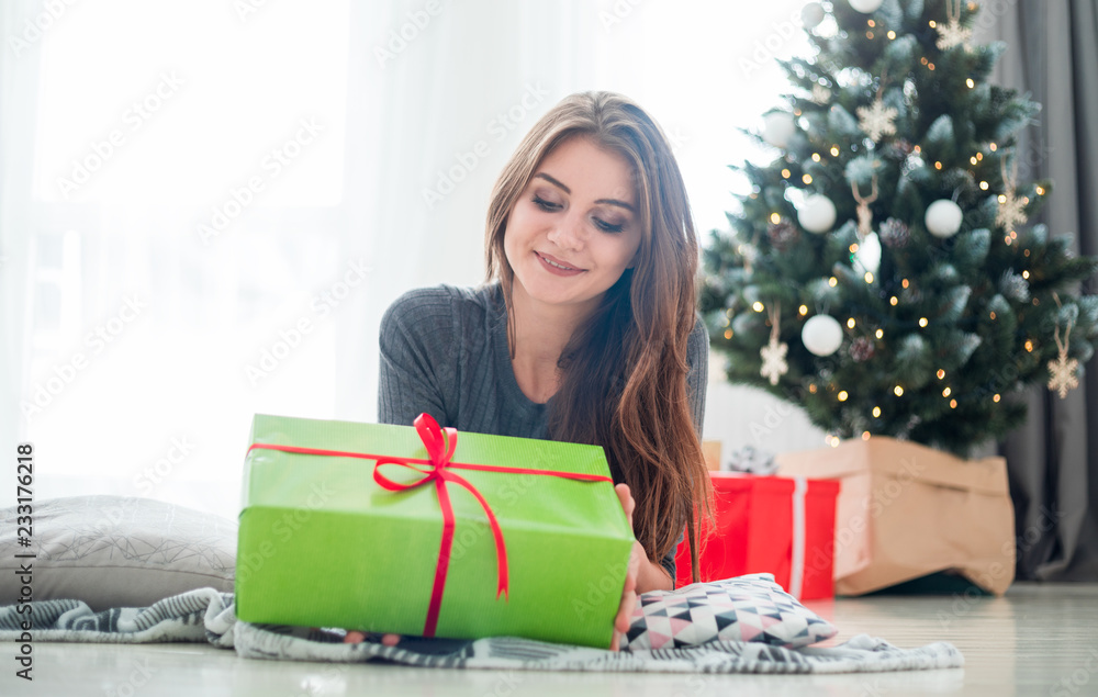 Cheerful young woman lying on floor surrounded by Xmas gifts next to Christmas tree Cheerful young woman lying on floor surrounded by Xmas gifts next to Christmas tree