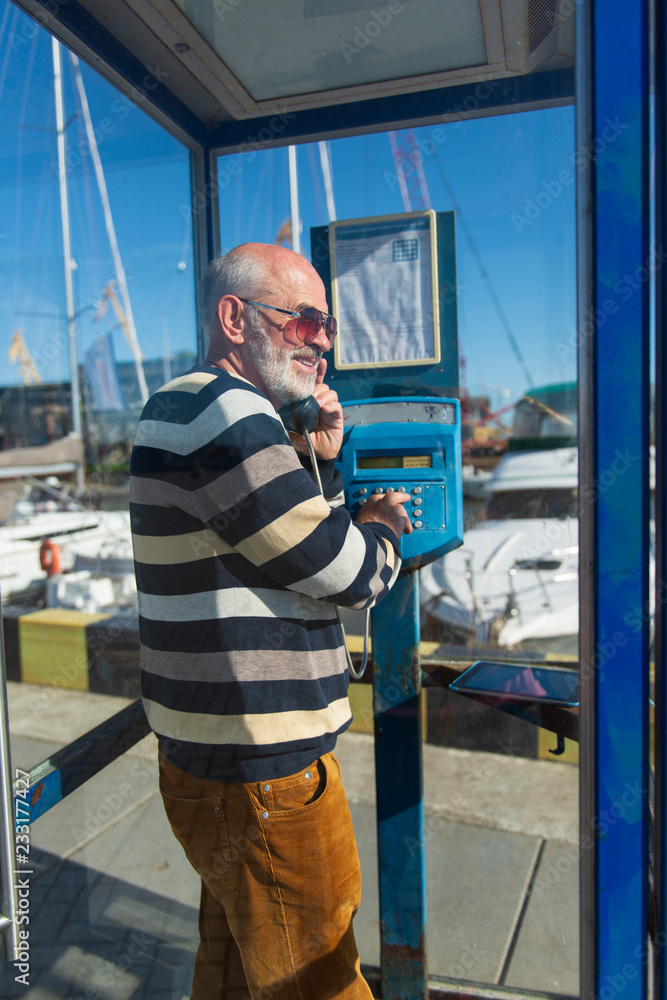 one old man makes a call from a blue payphone booth in a yacht port one old man makes a call from a blue payphone booth in a yacht port