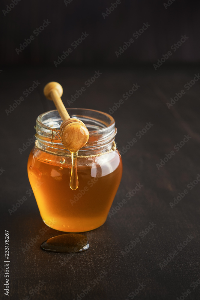 Honey in a glass jar with honey dipper on rustic wooden table background. Copy space. Honey in a glass jar with honey dipper on rustic wooden table background. Copy space.