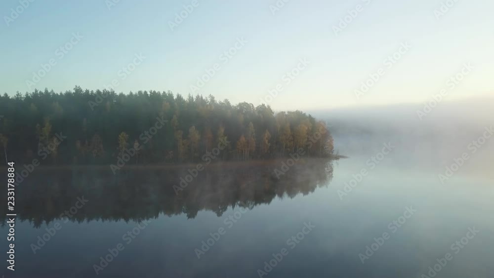 Aerial - Autumn misty morgning in sweden forest. sunrise hitting the trees. big lake in the middle. flying above the fog. 4k