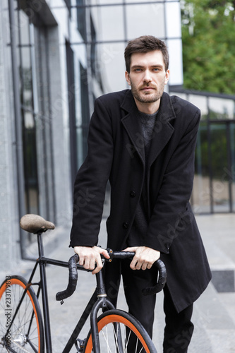 Handsome young business man walking outdoors with bicycle.