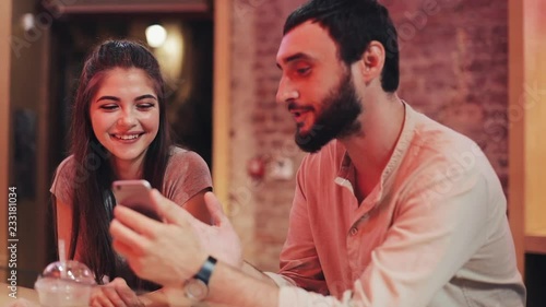 Beautiful Young Couple using Smartphone itting at the Bar. They win, a Sports Bet Gambling Win, Give Five photo