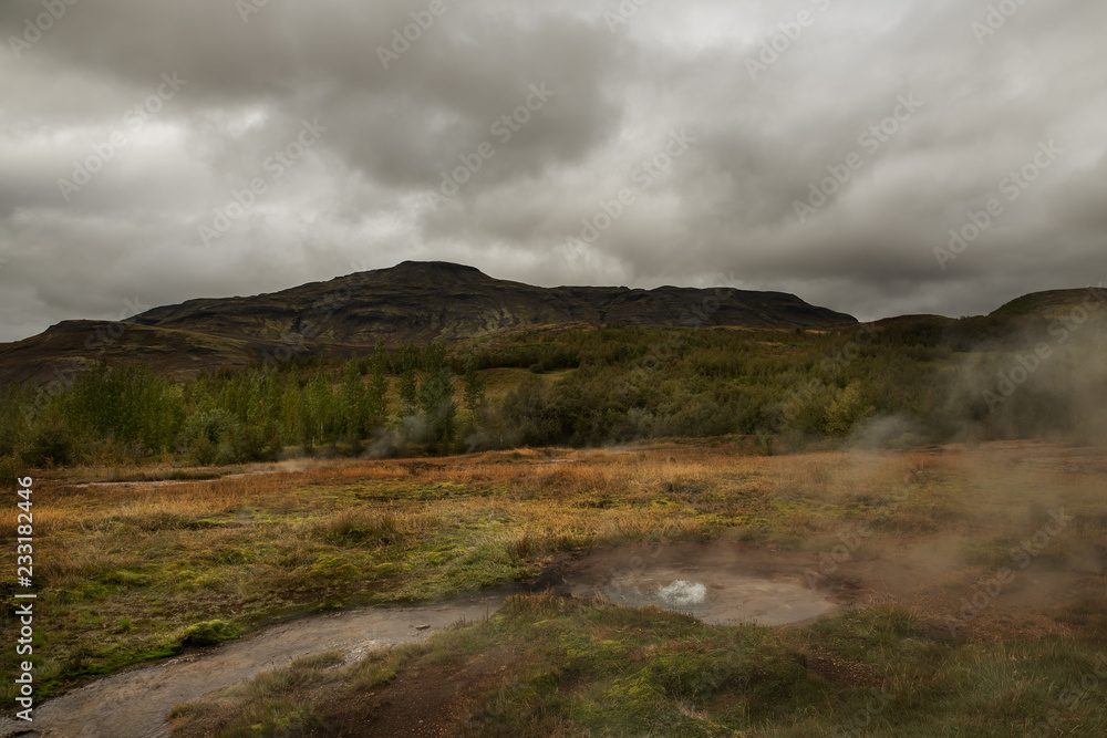 Icelandic landscape.Hot geyser spouting out of the ground on the hilly mountains.
