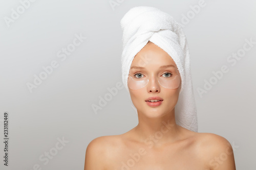 Portrait of pretty lady with white towel on head without makeup with transparent patches under eyes dreamily looking in camera over gray background isolated