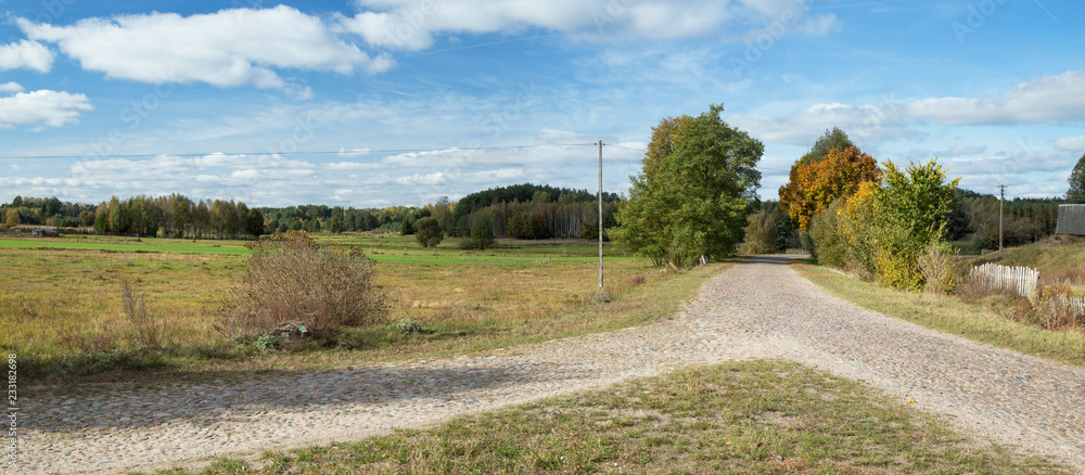 Crossing the old stone country road, you can see fields, a fence, a pillar and a nice blue sky with white clouds - Podlasie, Poland