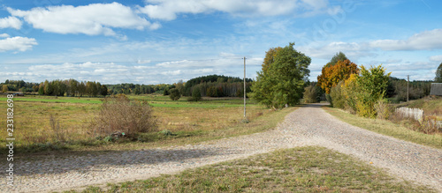 Crossing the old stone country road, you can see fields, a fence, a pillar and a nice blue sky with white clouds - Podlasie, Poland