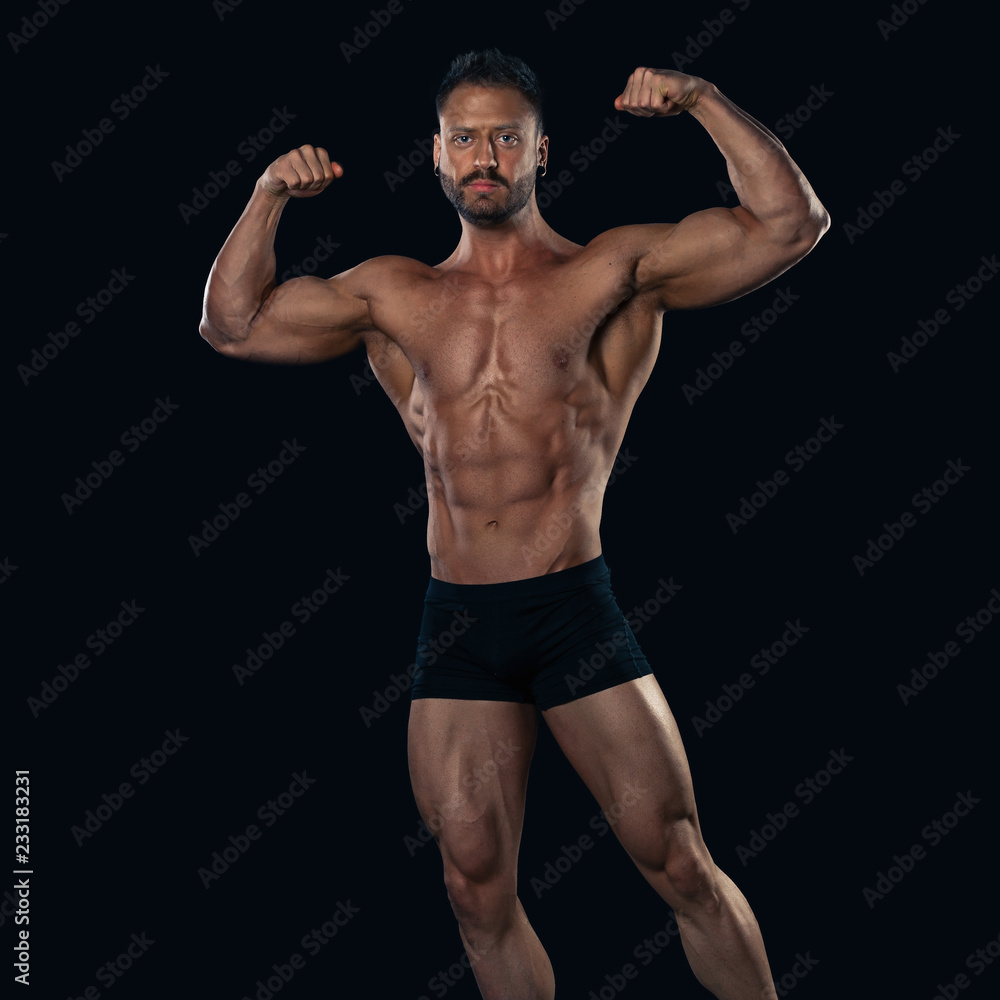 Brutal strong bodybuilder athletic man posing on black background.