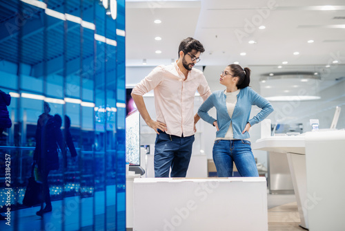 Young couple standing and discussing about smart TV they buying.