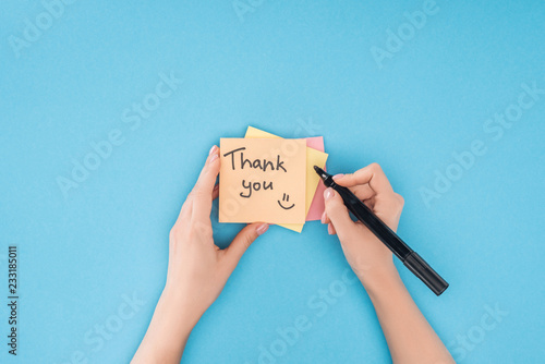 cropped person holding pen above colorful sticky notes with thank you lettering isolated on blue background photo