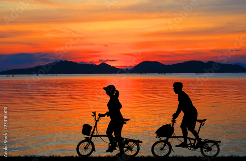 Silhouette couple and bike relaxing on blurry sunset background.