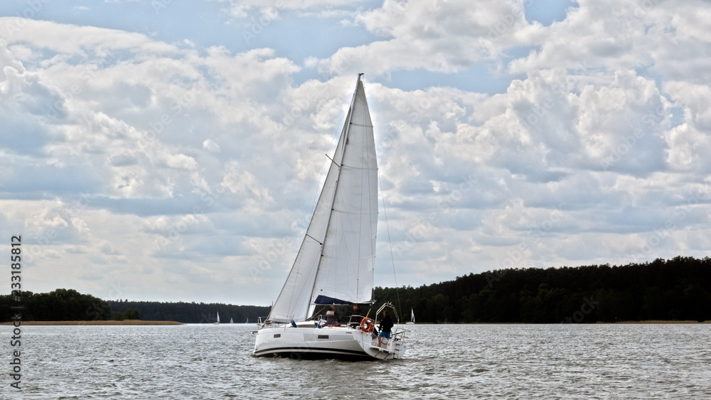 White boat sailing on the lake near Mikolajki, Poland under a cloudy sky. 