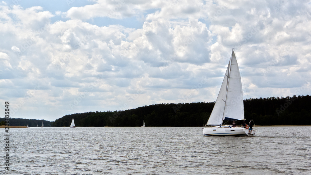 White boat sailing on the lake near Mikolajki, Poland under a cloudy sky. 