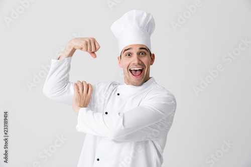 Excited young man chef indoors isolated over white wall background showing biceps.