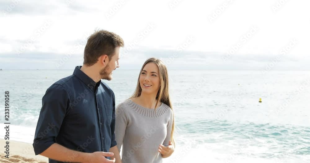 Happy couple walking and talking on the beach with the sea in the background Happy couple walking and talking on the beach with the sea in the background