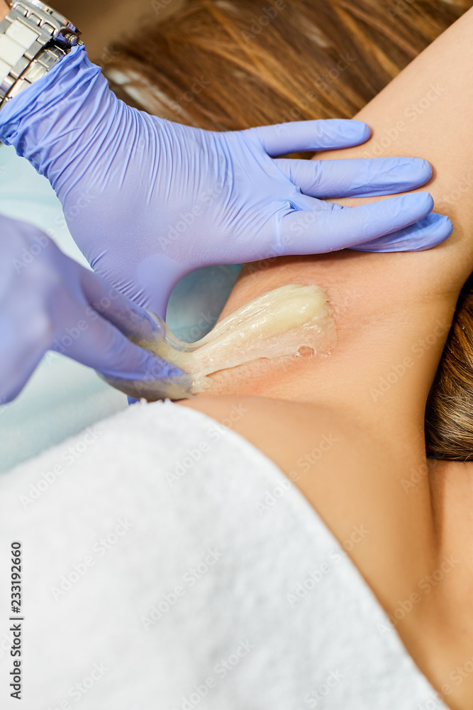 Naklejka premium The master of sugaring puts paste on the girl's armpits