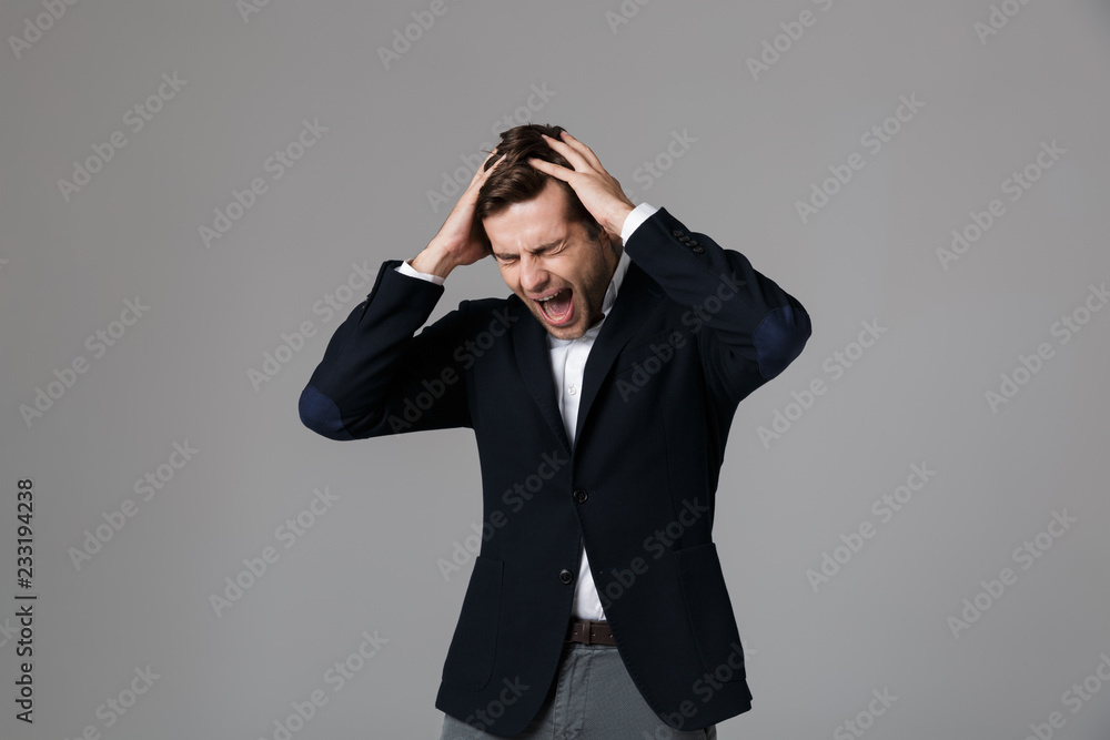 Image of puzzled businessman 30s in formal suit screaming and grabbing head, isolated over gray background Image of puzzled businessman 30s in formal suit screaming and grabbing head, isolated over gray background