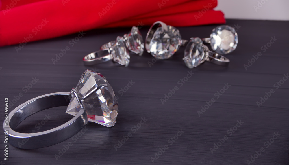Big diamond ring on the table. In the background a bunch of rings and red table napkin Big diamond ring on the table. In the background a bunch of rings and red table napkin