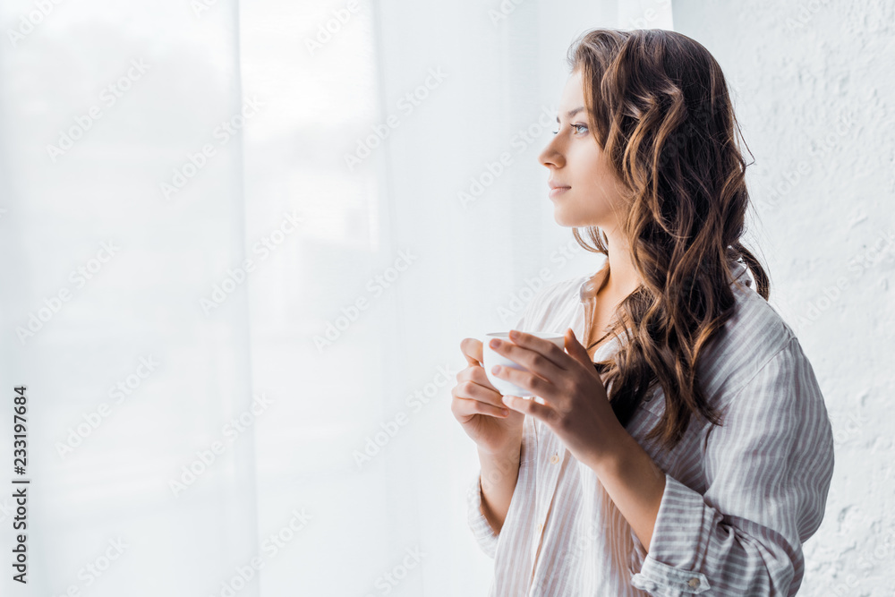 attractive girl standing with cup of coffee near window in the morning