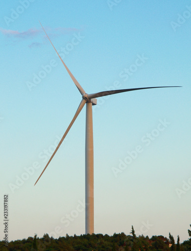 Isolated wind turbine at top of a hill, blue sky background