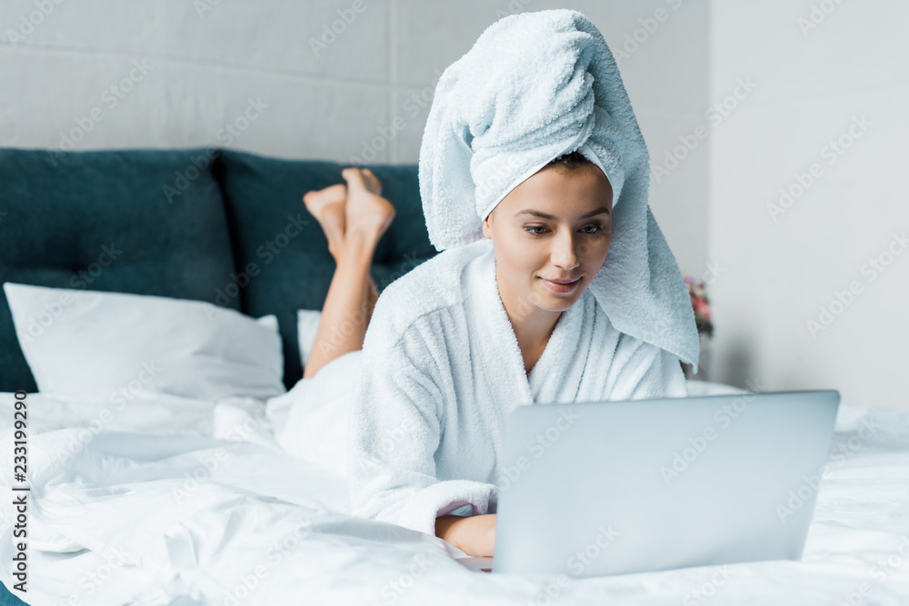beautiful young woman in bathrobe using laptop while lying on bed in the morning beautiful young woman in bathrobe using laptop while lying on bed in the morning