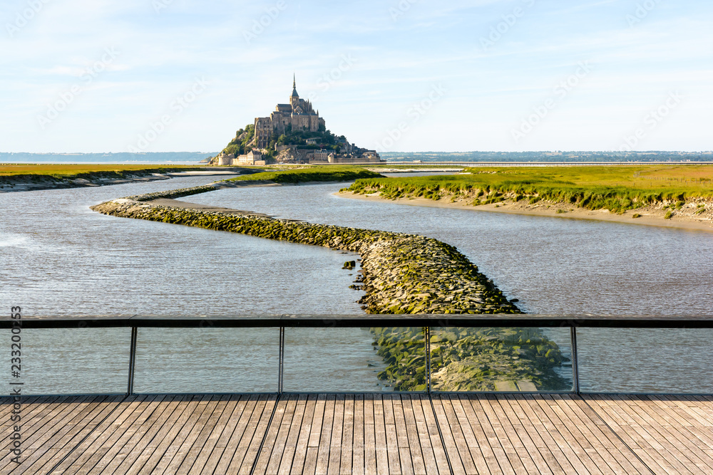 Φωτογραφία View of the Mont Saint-Michel tidal island, located in France on the limit between Normandy and Brittany, at high tide with the wooden footbridge over the dam on the Couesnon river in the foreground