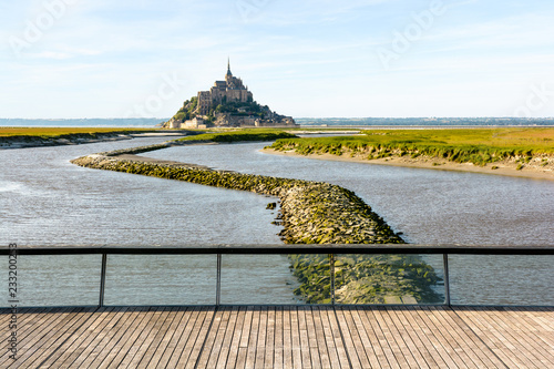 Canvas Print View of the Mont Saint-Michel tidal island, located in France on the limit between Normandy and Brittany, at high tide with the wooden footbridge over the dam on the Couesnon river in the foreground