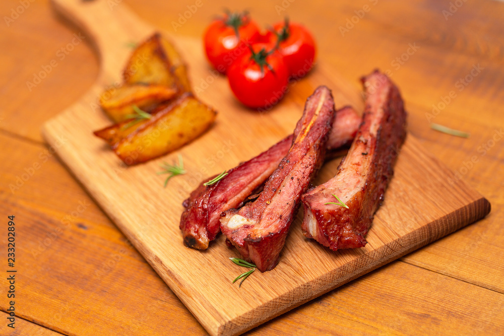 Pork ribs served with tomato and fried potato on wooden table.