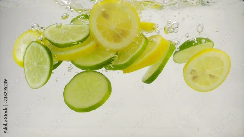 Slices of citrus lime and lemon fall into the water with splashes and bubbles, slow motion close-up