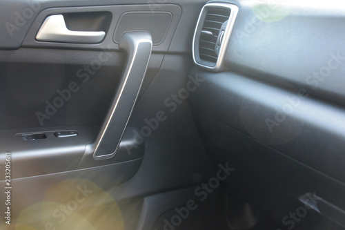 Car indoor. Black plastic automobile door with chrome details, buttons and air grid, part of door handle with blurred colorful bokeh on front