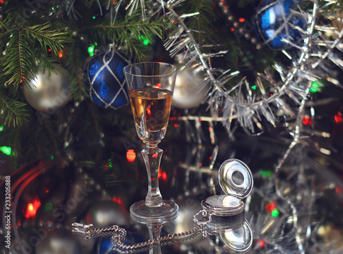 A glass of wine and antique silver clocks next to the fir branches decorated with tinsel and multi-colored glass balls. © elena_p