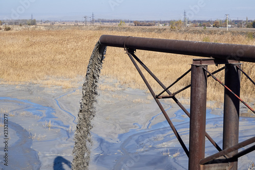 a gray mass of swill flows through a rusty pipe from a height of a pipe into a polluted lake
