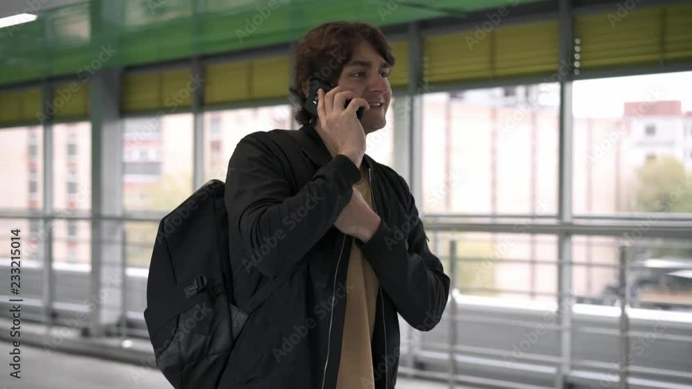 Side view of caucasian young man wearing black jacket walking in tunnel and talking on his smartphone Tracking real time medium shot Side view of caucasian young man wearing black jacket walking in tunnel and talking on his smartphone Tracking real time medium shot