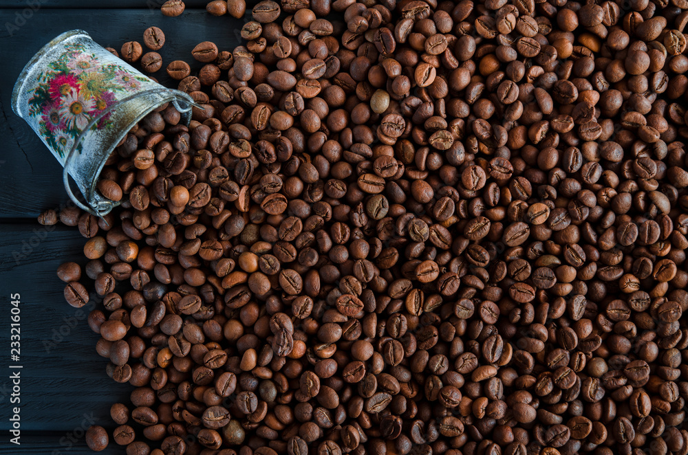 Fototapeta premium Roasted fragrant grains of black coffee are scattered from a white metal bucket on a black table
