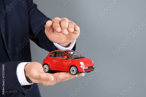 Male insurance agent holding toy car on grey background, closeup. Space for text