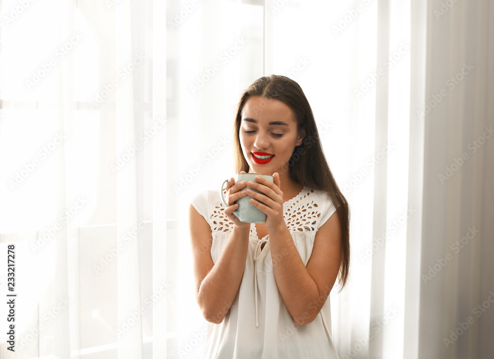 Young woman standing near window with beautiful curtains at home Young woman standing near window with beautiful curtains at home