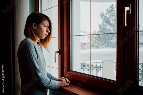 Sad woman sitting by the window looking outside