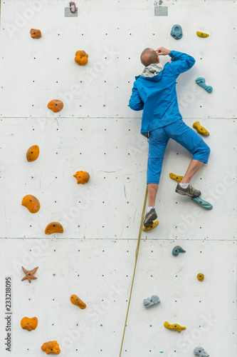 Young Man Climbs Up An Artificial Rock Wall, sport and fitness concept. Sporty man practicing rock climbing in climbing gym. vertical photo.